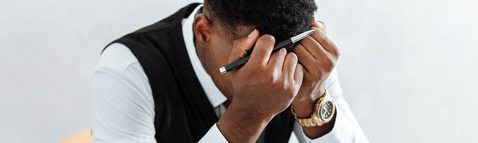 A young writer wearing an official cloth bows in his hands with regrets. He has a writing note, a desk, and laptop in front of him.