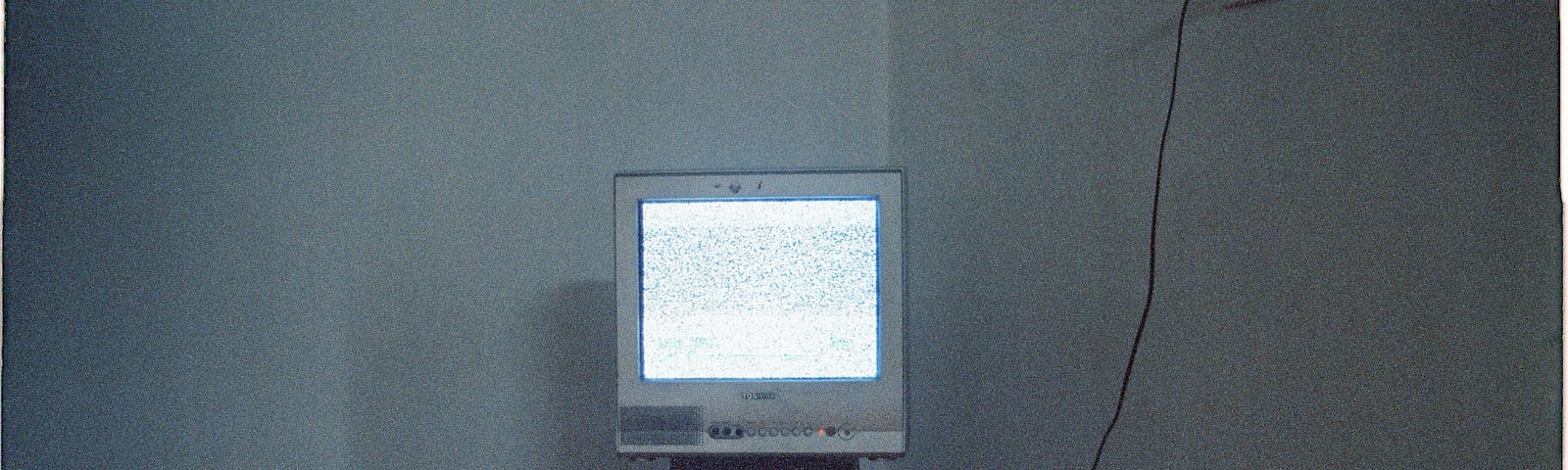 An old-fashioned tube television in the corner of a room, sitting on a stool and plugged into an outlet high on the wall.