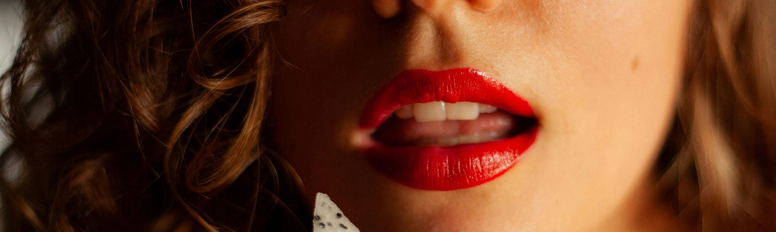 A close up image of a woman with red lips about to eat a piece of dragon fruit.