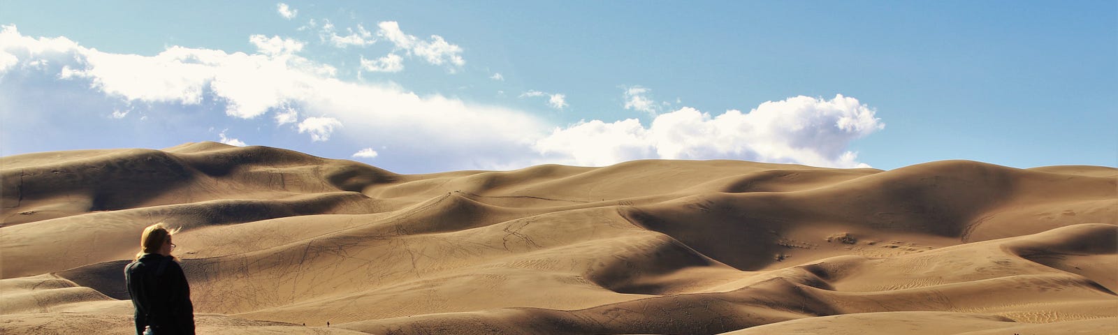 A woman stands in front of sand dunes