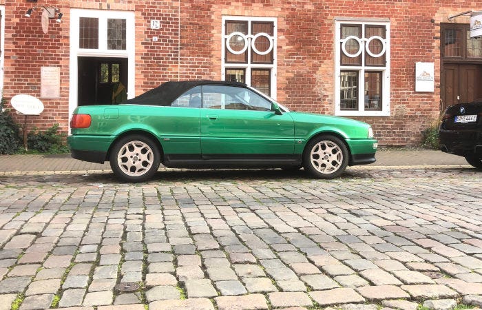 Metallic green soft top car on cobblestone road in Potsdam