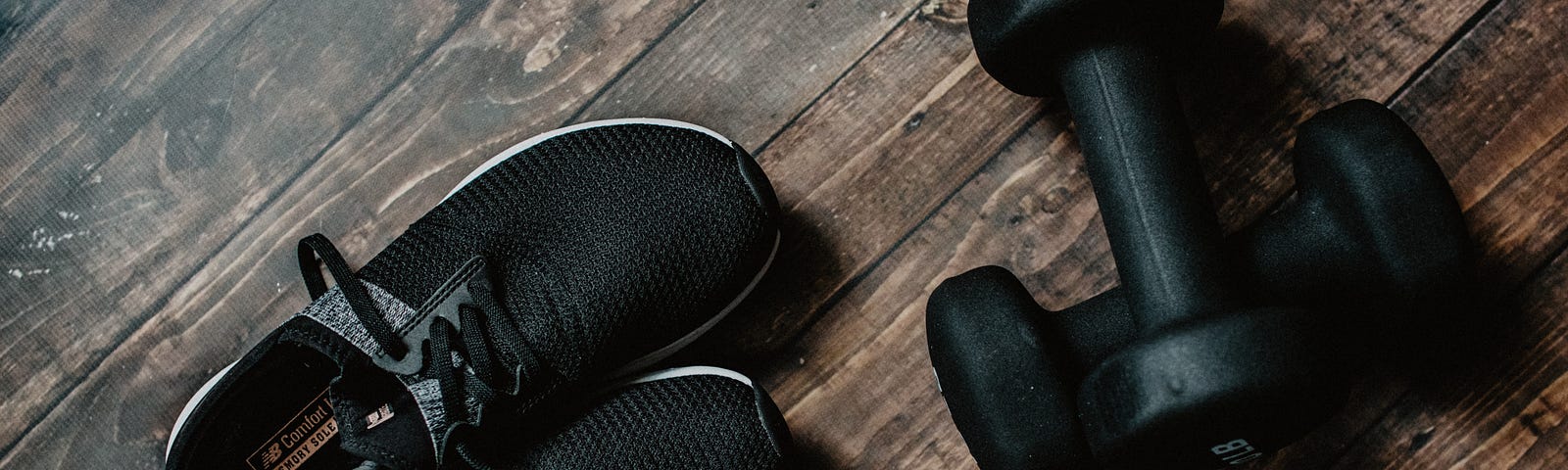 Black sneakers and hand weights on a wooden floor