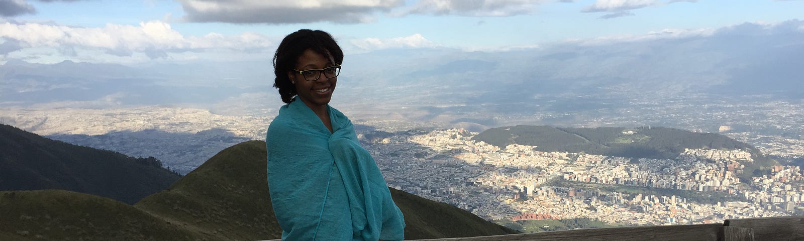 Aneisha standing in front of a mountain in Ecuador wearing a blue shawl.