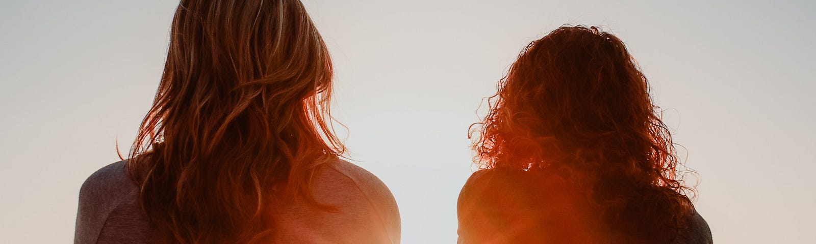 Two women sitting on beach looking at sunset