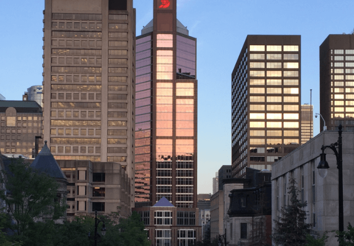 Cityscape at sunset with reddish light reflecting off glass-fronted buildings