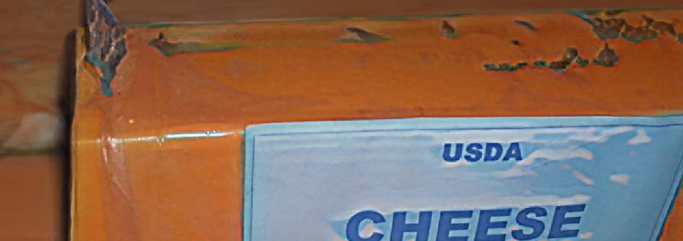 An orange package of USDA government cheese on a wooden table.