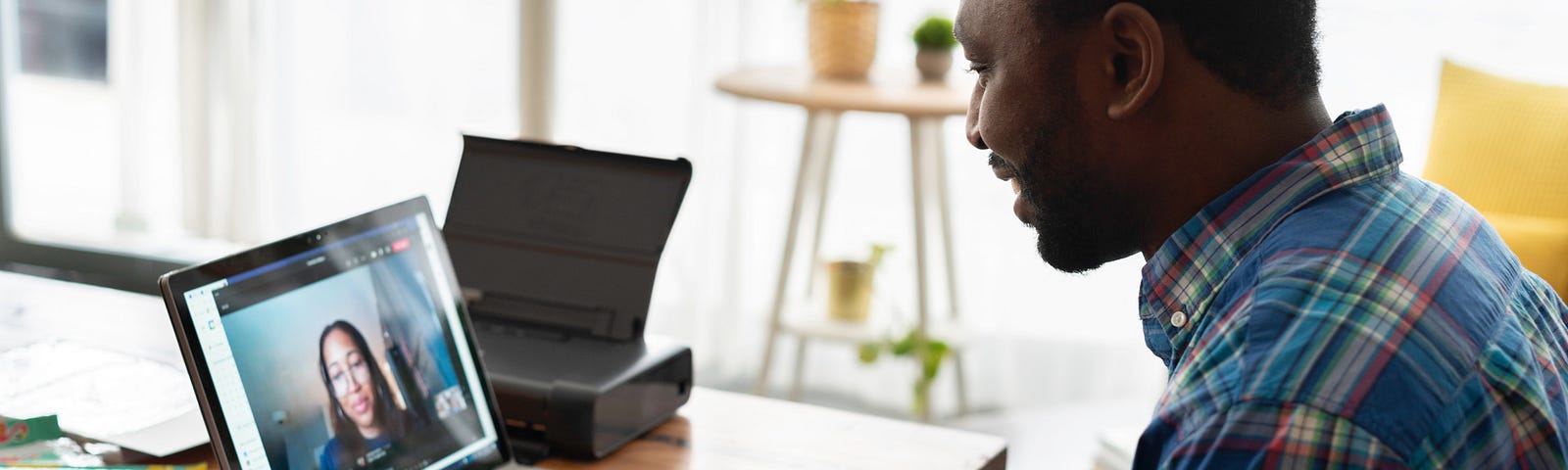 Homem negro em frente ao computador sentado, conversando com uma mulher. O computador está sobre a mesa