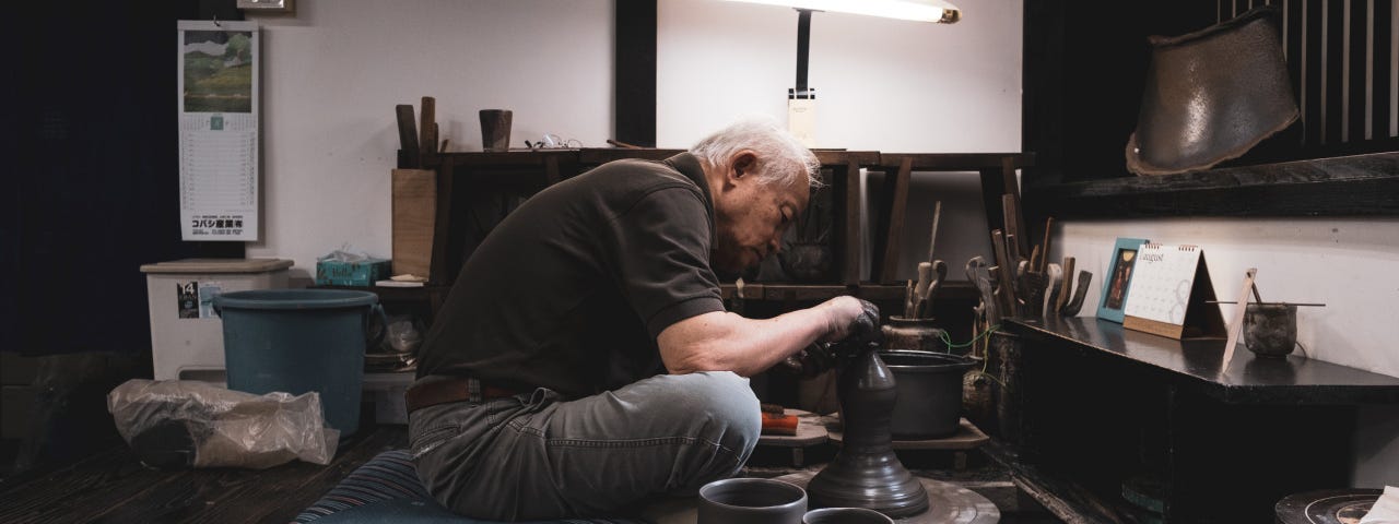 A master Japanese potter makes clay cups at his wheel.