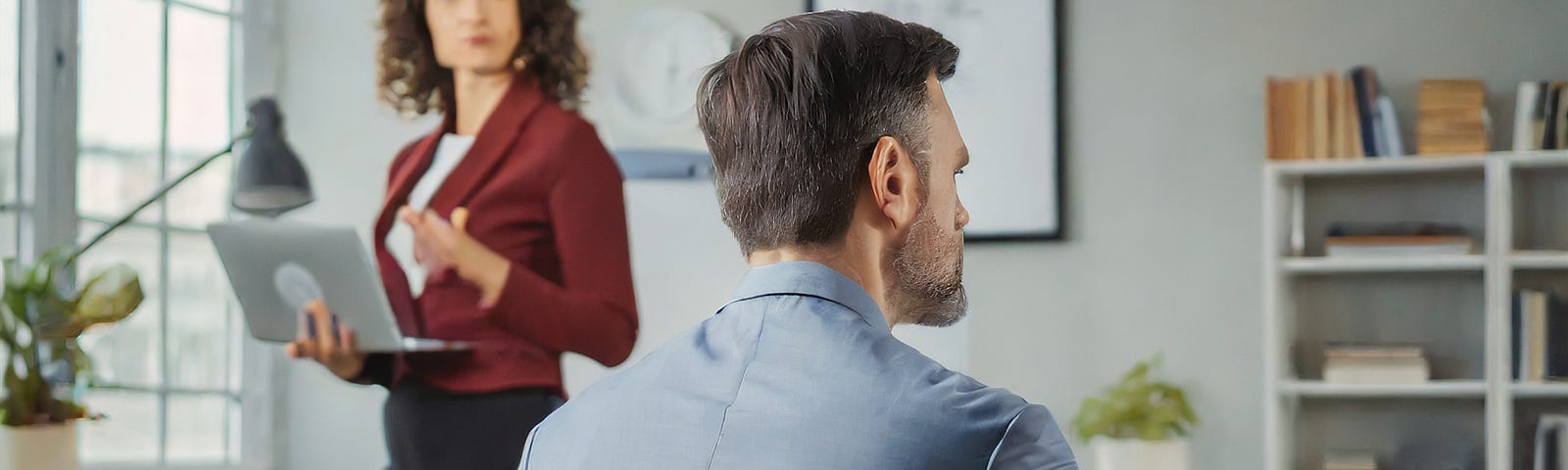 An unhappy woman turns her back to walk away from a man who is working on his laptop, while sitting at his desk and ignoring her. She is unhappy, but determined. both people are in their 40s and attractive.