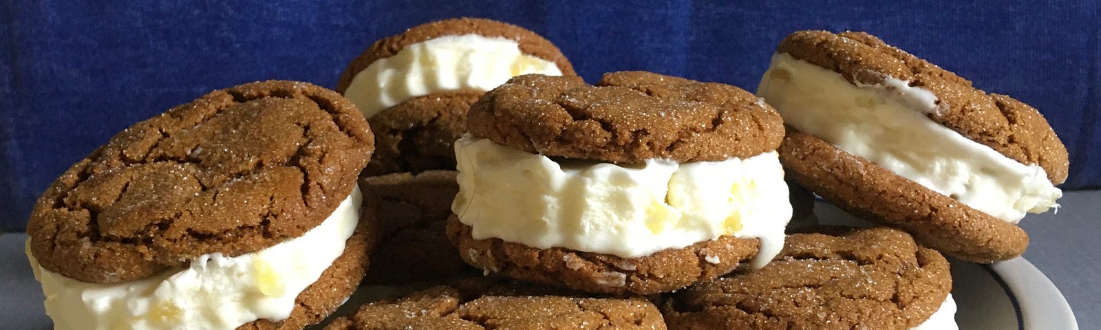 A white platter piled high with ice cream sandwiches made with ginger cookies.