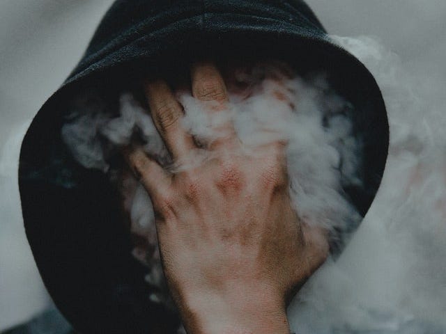 person in black hoodie with hand over face and smoke