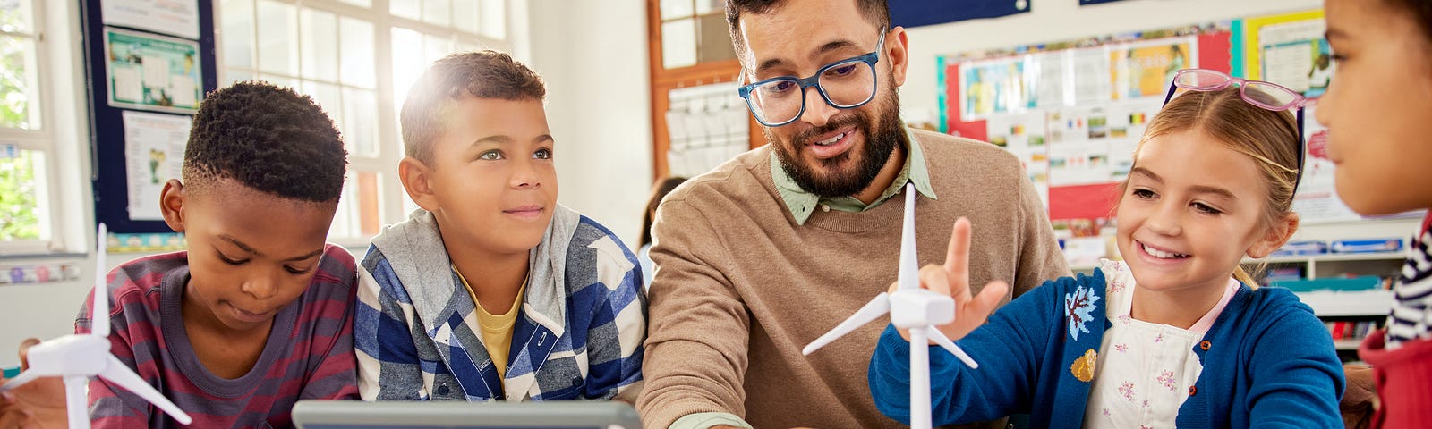 Male teacher explaining wind turbines in science class during primary school lesson.