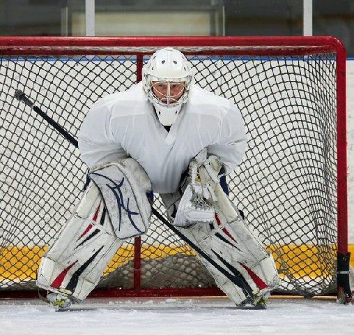 A photo of a hockey goaltender standing in front of ais goal.