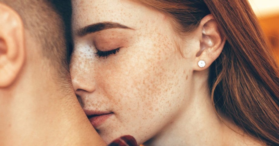 A beautiful girl with freckles with her face up against a guy's neck