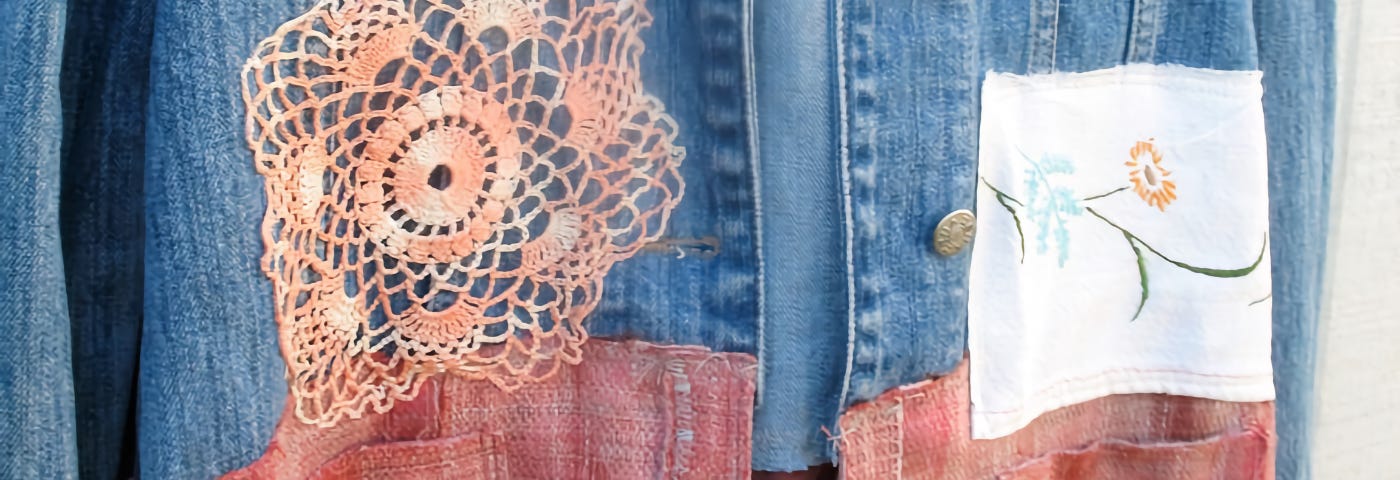 A denim jacket with an orange flower patch, a white square patch with a flower print, and a reddish-orange patch over the bottom half of the jacket.
