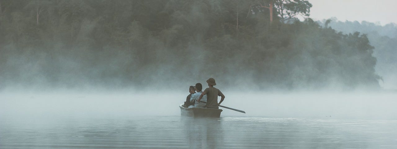 Three boys rowing on the river in a rowboat as they head into the mist.