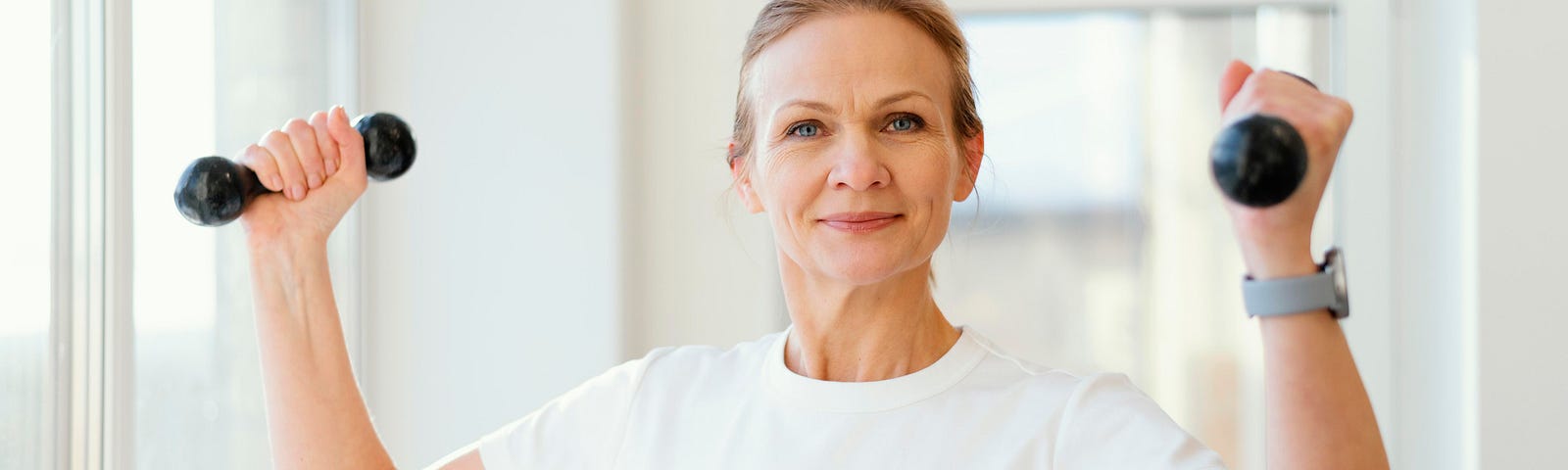 Mature woman wearing a white T-shirt holding small hand weights.