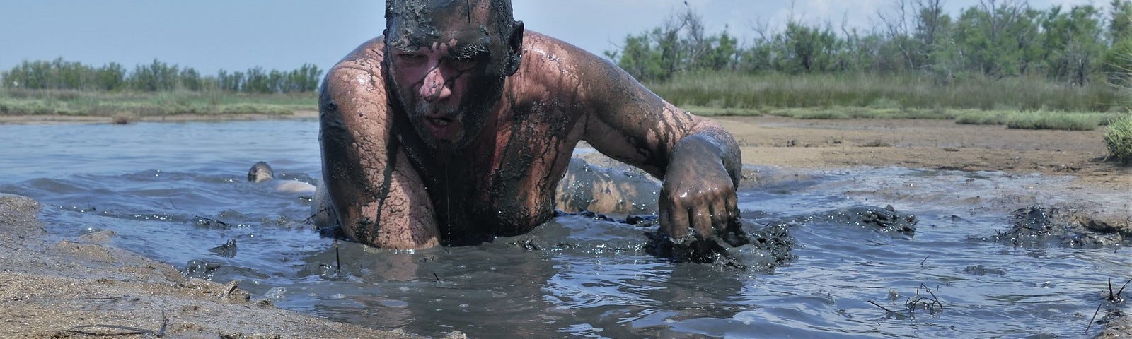 A very muddy man in a stream