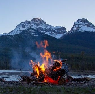 Campfire burning with snow-capped mountain peaks in the distance