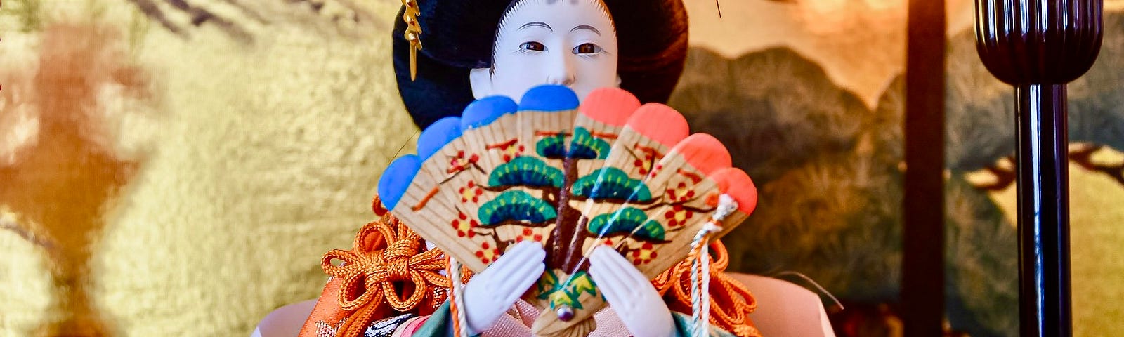 Empress Hina doll, face partially covered by a folding fan she is holding.