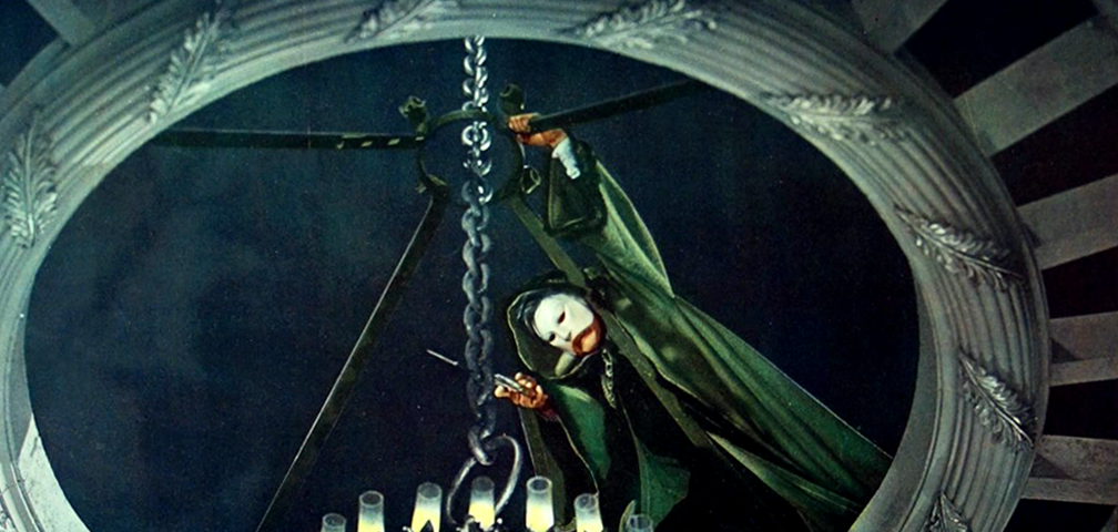 Film still from 1943’s Phantom of the Opera where masked title character is in opening above chandelier, sawing its chain.