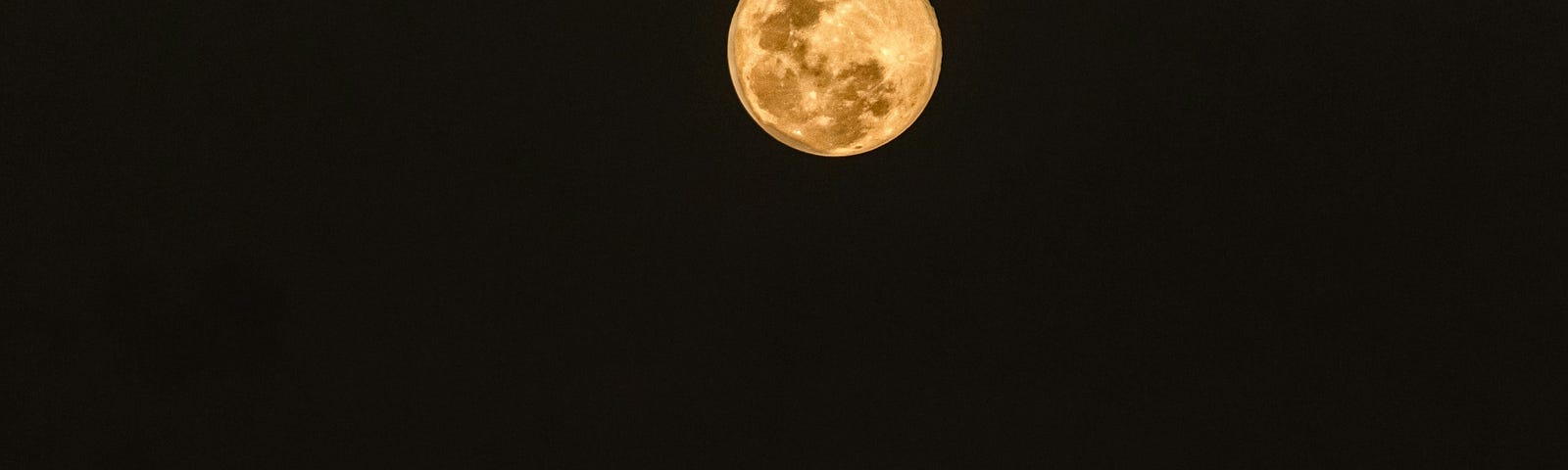 Large full moon shining on water at night.