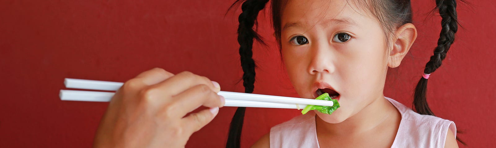mother-feeding-vegetable-her-daughter-high-chair-against-red-wall-background — Un Swede