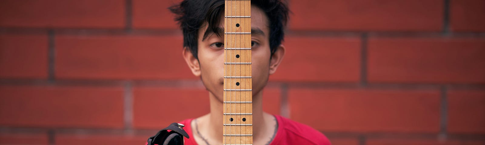 A musician holding up his guitar so it divides one side of his face from the other