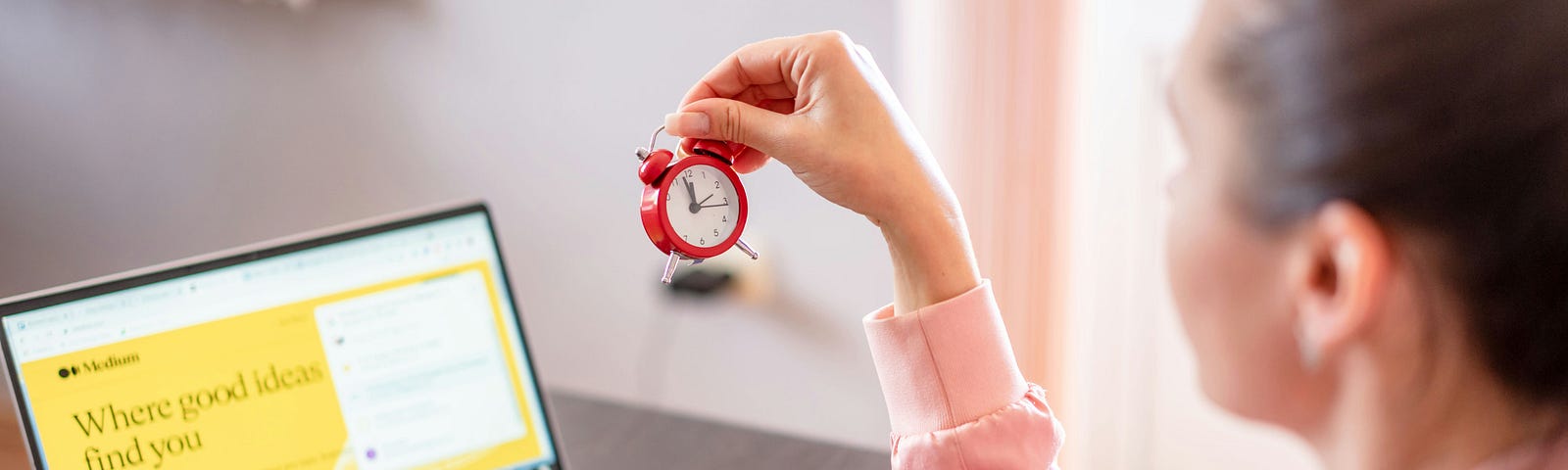 a woman at her laptop examines an alarm clock