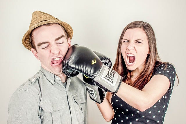 Photo of a woman wearing boxing gloves jabbing a man in the face.