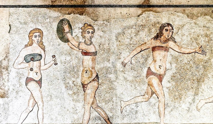 Mosaic portraying three young girls wearing what look like bikinis: one is holding small dumbbells, one is in the act of throwing a discus, the other is running. Two of the girls have blonde hair, the third has brown hair. The discus throwing girl is wearing golden bracelets, necklace and ankle bracelets