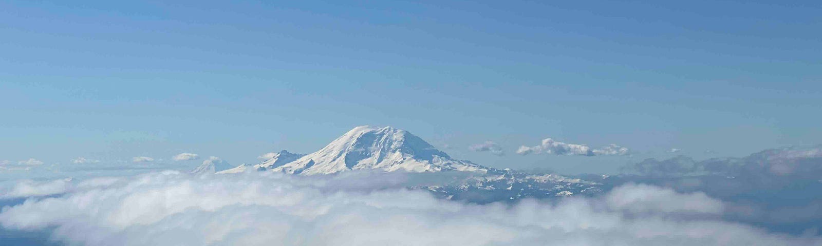 Snow-covered mountain peak of Mount Rainier rising above the clouds