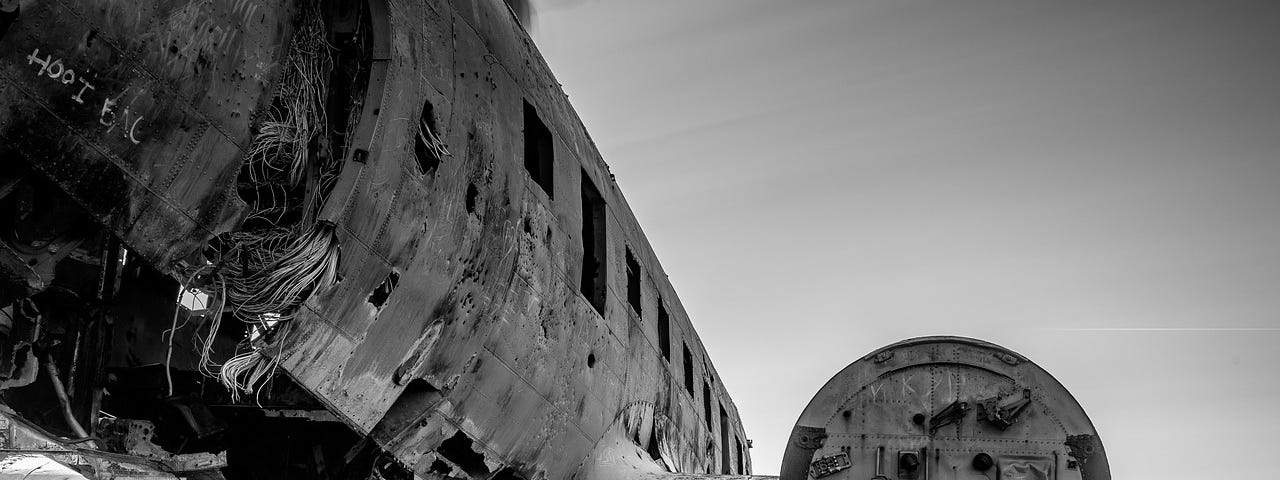 Black-and-white image shows the side of a crashed plane, and the engine on what’s left of its wing.