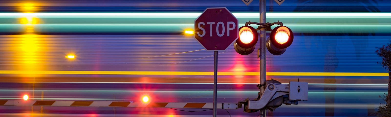 Night scene, light blur of train passing by. Stop sign and railroad crossing with barrier down.