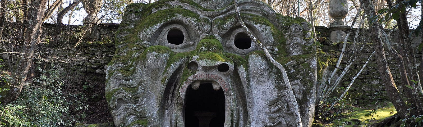 Doorway into the underworld. Stone stairs lead to a moss covered, carved open mouth doorway and bulging eyes. This is considered a carving of “Orcus”.
