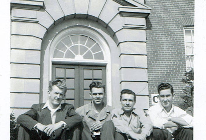A photo of four men sitting in front of a building during the 1940s.