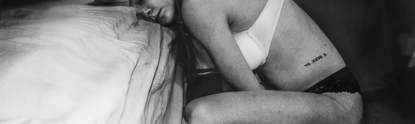 Woman leaning her head against the bed and holding her stomach