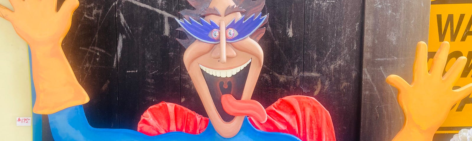 A cardboard cutout of a silly cartoon superhero having yellow gloves, a blue outfit and red cape