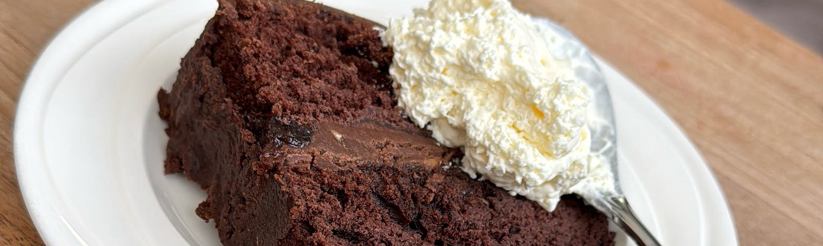 Devil’s Food Chocolate Cake, on white plate, with a spoon with whipped cream on it