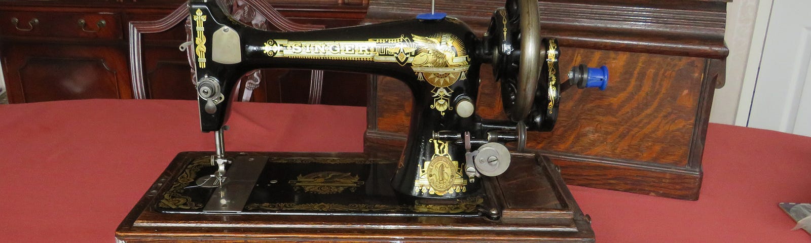 A classic hand-cranked Singer sewing machine in black with a gold decal of a sphinx, and all the attachments.