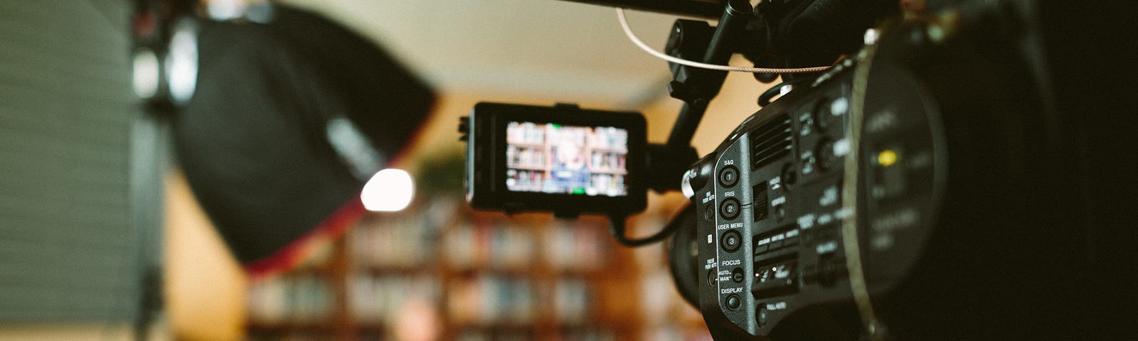 A camera pointed to a live set in a library. The host is sitting in a sofa.