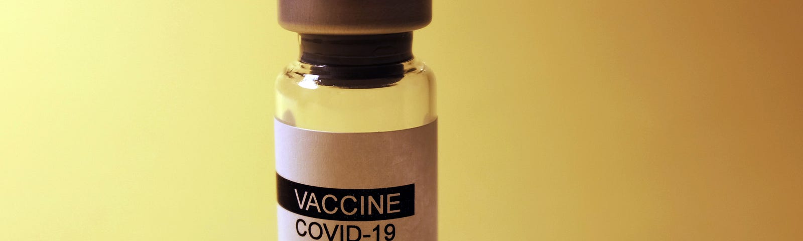 Picture of a COVID-19 vaccine bottle against a yellow background.