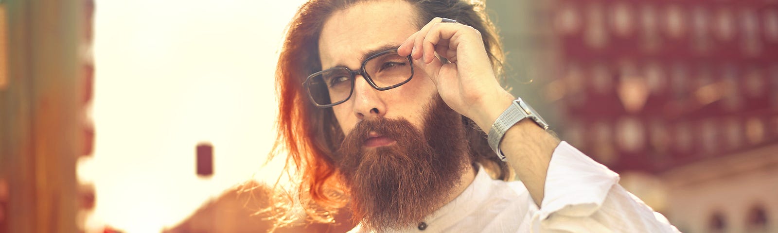 Stylish man in a white buttoned shirt with a full beard, long hair, and spectacles