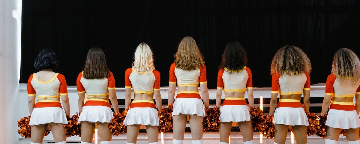 Seven cheerleaders standing in a line with their backs to the camera.
