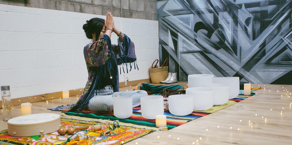 A woman sitting cross-legged on a colorful blanket with her hands folded together on her forehead — spiritual.