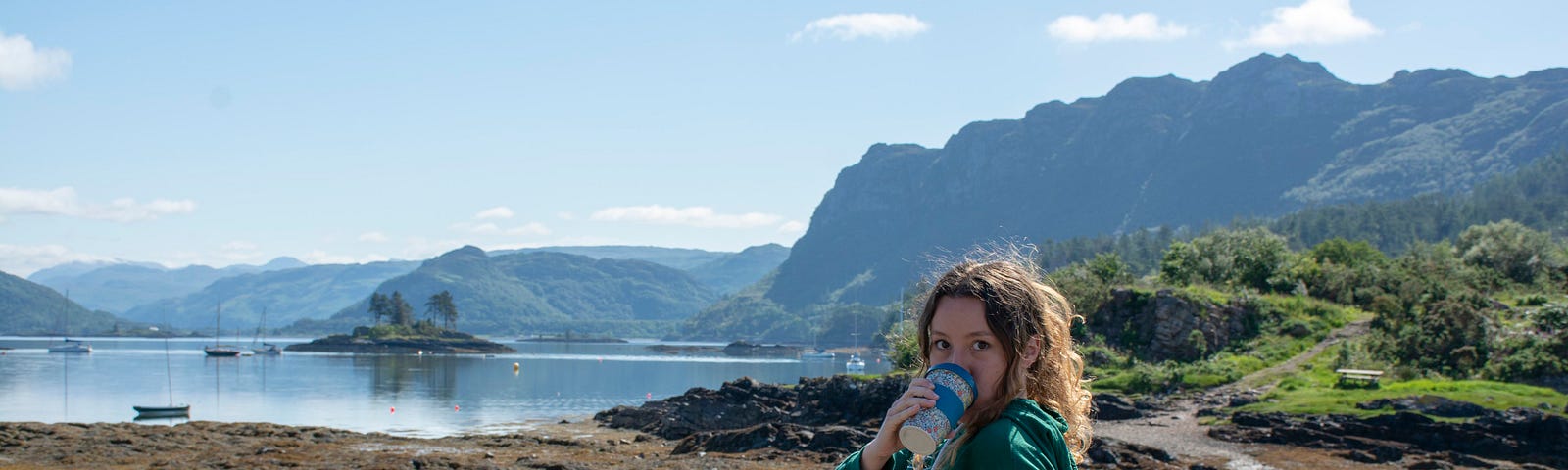 a young woman drinking coffee, a lake and mountains in the background