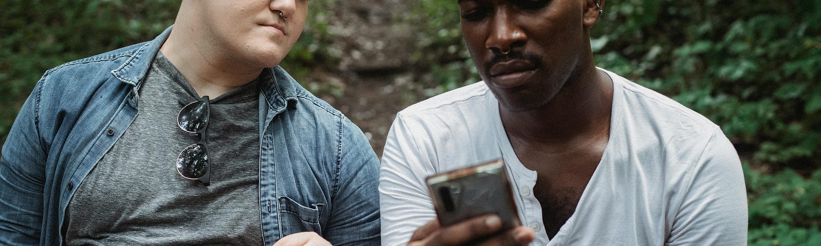 Pensive friends browsing smartphone in forest in daytime