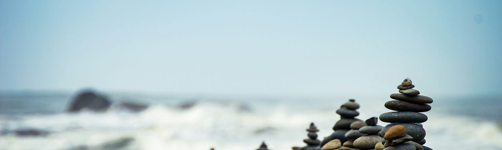 Rocks stacked in order of size on top of boulder, with ocean waves in the backgroud.