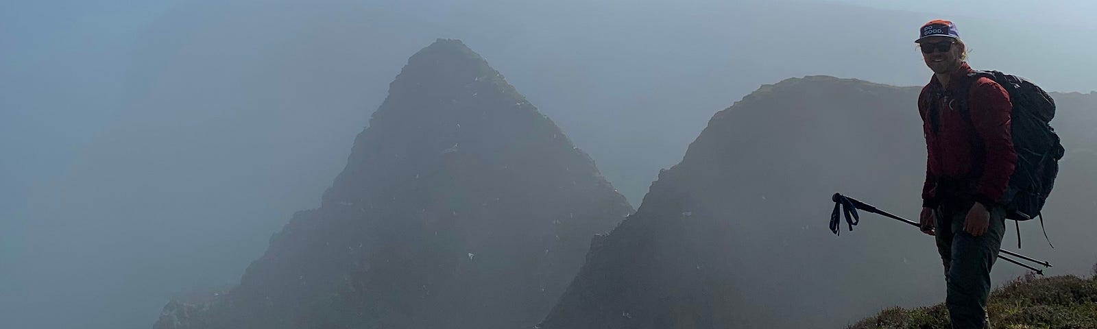 A man stands before sea stacks looming like mountains in the mist.