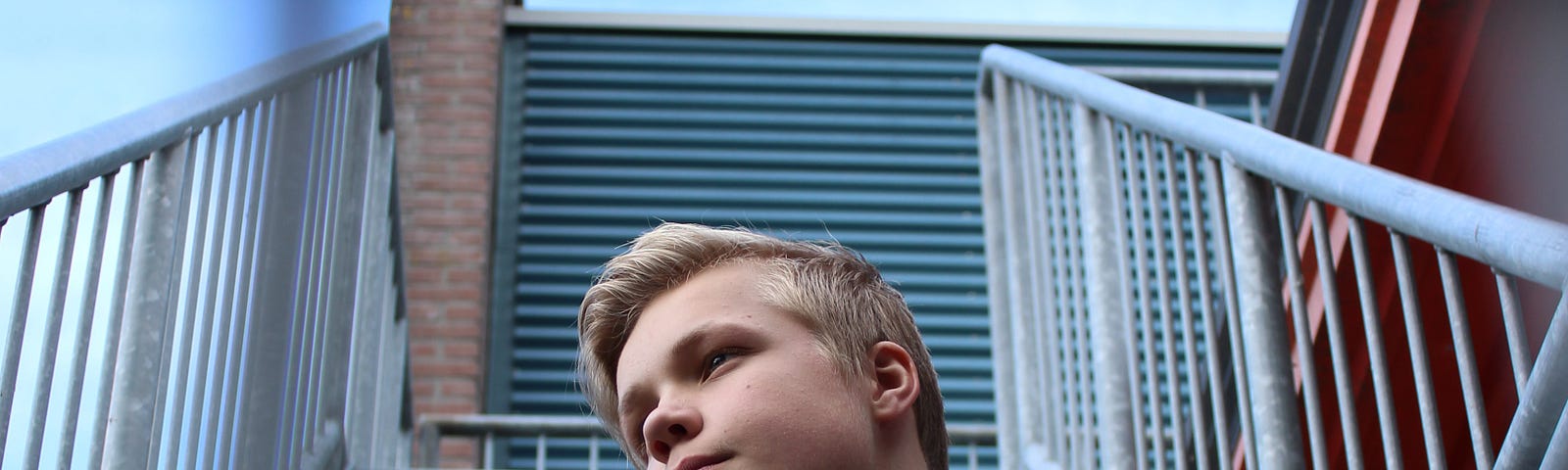 Young blonde boy sitting on concrete stairs.
